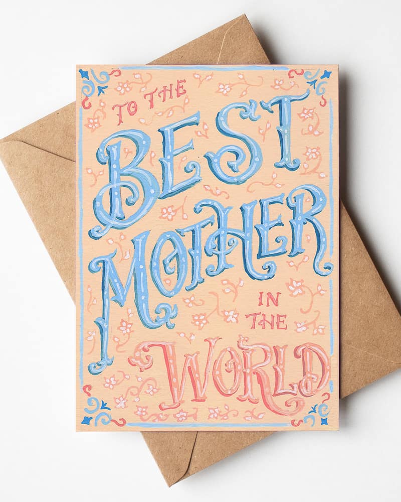 Hand-lettered Mother's Day card which reads, "To the best Mother in the World" in Victorian lettering. "Best Mother" is in blue and the other words and decorative flower elements are in a peach color.