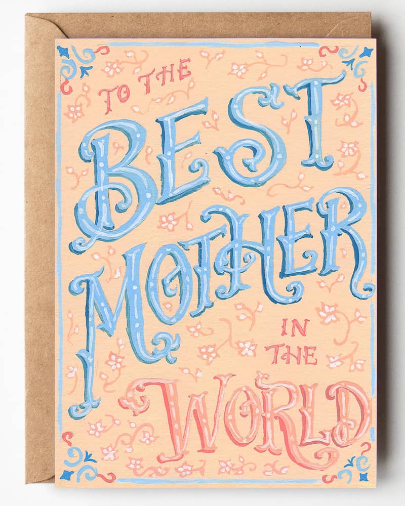 Hand-lettered Mother's Day card which reads, "To the best Mother in the World" in Victorian lettering. "Best Mother" is in blue and the other words and decorative flower elements are in a peach color.