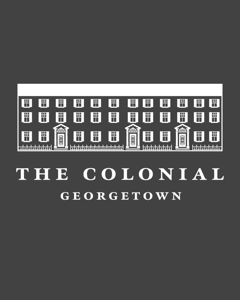 A white logo on charcoal gray background featuring a line drawing of a Colonial-style historic building with three doors and many windows. In elegant serif type it says "The Colonial Georgetown".