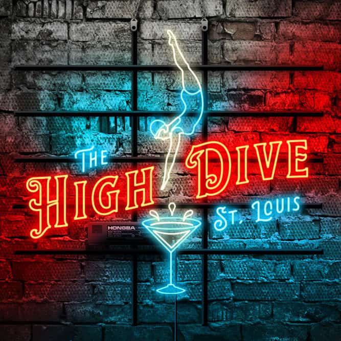 Red, turquoise blue, and warm white neon sign for the High Dive bar that says The High Dive St. Louis and shows a woman in a blue bathing suit and cap diving info a martini glass. High Dive is in red neon. The neon is glowing against a brick wall.